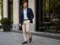 Elegancki mężczyzna w jasnych chinosach i granatowej marynarce spaceruje po mieście.