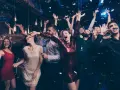 Impreza w pełni! Ludzie tańczą, rzucają konfetti, a ich stroje idealnie pasują do **dress code'u na imprezę**.