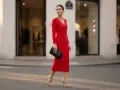 Elegancka kobieta w czerwonej sukience i szpilkach, niosąca czarną kopertówkę. Stylowe stylizacje z czerwoną sukienką na ulicach miasta.