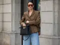 Eleganckie jeansy i brązowa marynarka damska tworzą stylową, miejską stylizację. Kobieta trzyma czarną torebkę.