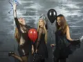 Trzy dziewczyny w sukienkach na imprezie, z balonami i konfetti. Inspiracja, jak ubrać się na 18 jako gość.