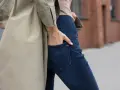 Kobieta w beżowym płaszczu i granatowych jeansach bootcut. Stylowe jeansy bootcut to podstawa wielu udanych stylizacji.