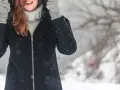 Kobieta w zimowej kurtce i rękawiczkach, zastanawia się, czy płaszcz z alpaki można prać w pralce. Śnieg pada wokół.