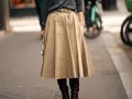 Eleganckie stylizacje ze spódnicą: beżowa, rozkloszowana spódnica midi, szary sweter i brązowe kozaki.