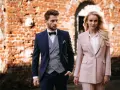 Elegancka para w strojach na komunię dziecka. On w granatowym garniturze, ona w pudrowym.