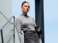 Elegancka kobieta w szarym golfie i jeansach, z czarną torebką, prezentuje styl **business casual** na tle nowoczesnej architektury.