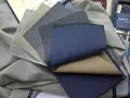 Próbki tkanin wełnianych w odcieniach szarości i niebieskiego, niektóre z subtelnym prążkiem.