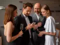 Elegancka kobieta w białej sukni i mężczyzna w czarnym smokingu dyskutują, co założyć na sukienkę wieczorową, trzymając telefony i kieliszki.