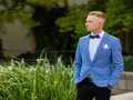 Elegancki mężczyzna w niebieskiej marynarce i czarnych spodniach, z muszką. Idealna stylizacja, jak ubrać faceta na wesele bez garnituru.