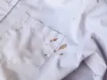 Biała koszula z widocznymi, niedopranymi plamami z błota na kieszeni i rękawie.