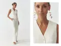 Elegancka kobieta w białej kamizelce bez marynarki i spodniach. Długie, złote kolczyki dodają stylizacji szyku.