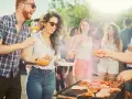 Ludzie cieszą się grillem w słoneczny dzień. Wszyscy ubrani są swobodnie, idealnie na grilla: koszule w kratę, jeansy, szorty.