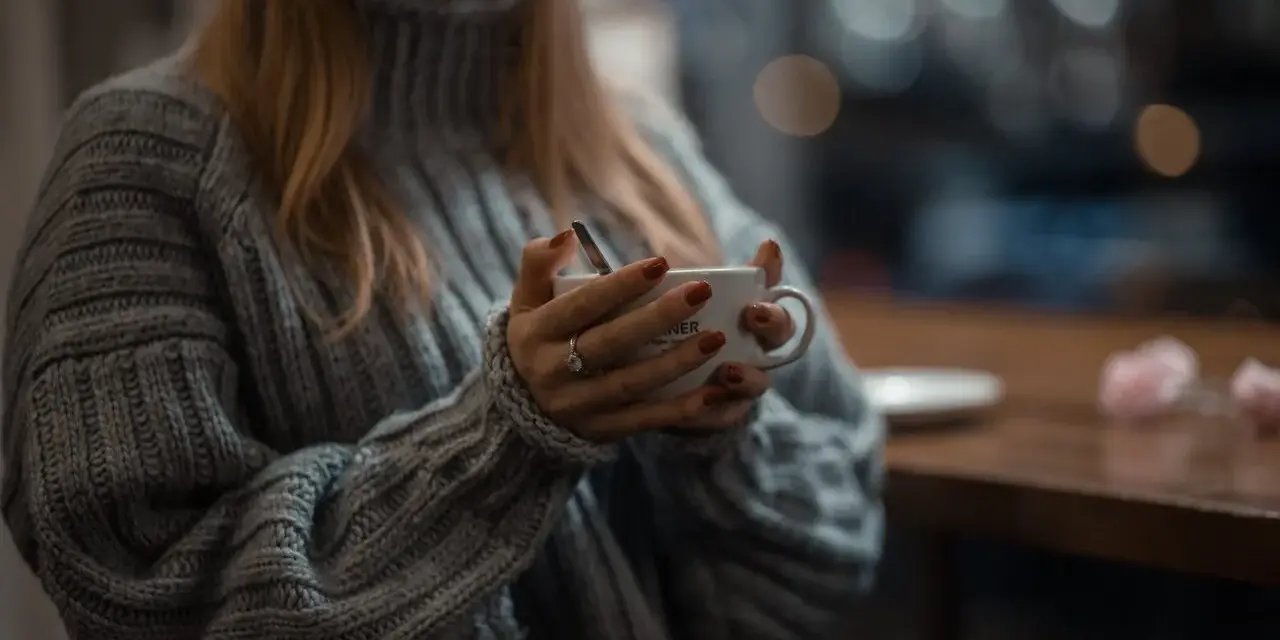 Mięciutki sweter z **lambswool** otula dłonie trzymające kubek. Czy taki materiał **gryzie**? Raczej nie, wygląda na bardzo komfortowy.