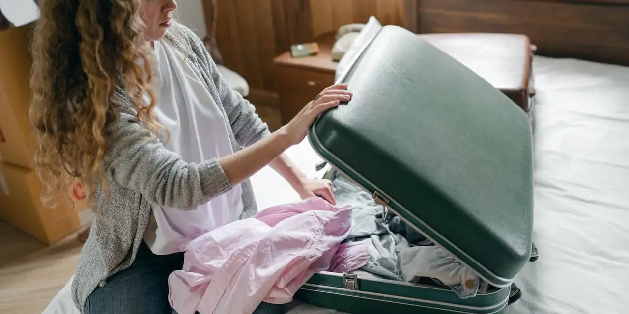 Kobieta pakuje różową koszulę do zielonej walizki, ucząc się, jak złożyć koszulę do walizki, by zaoszczędzić miejsce.