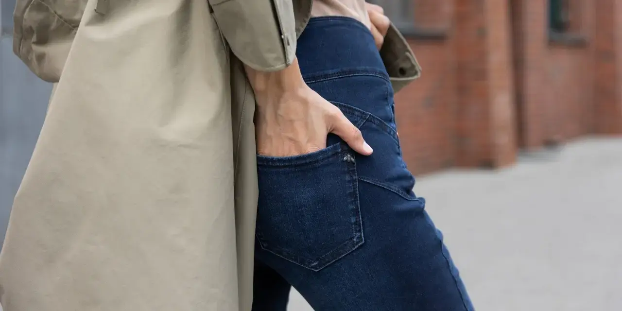 Kobieta w beżowym płaszczu i granatowych jeansach bootcut. Stylowe jeansy bootcut to podstawa wielu udanych stylizacji.