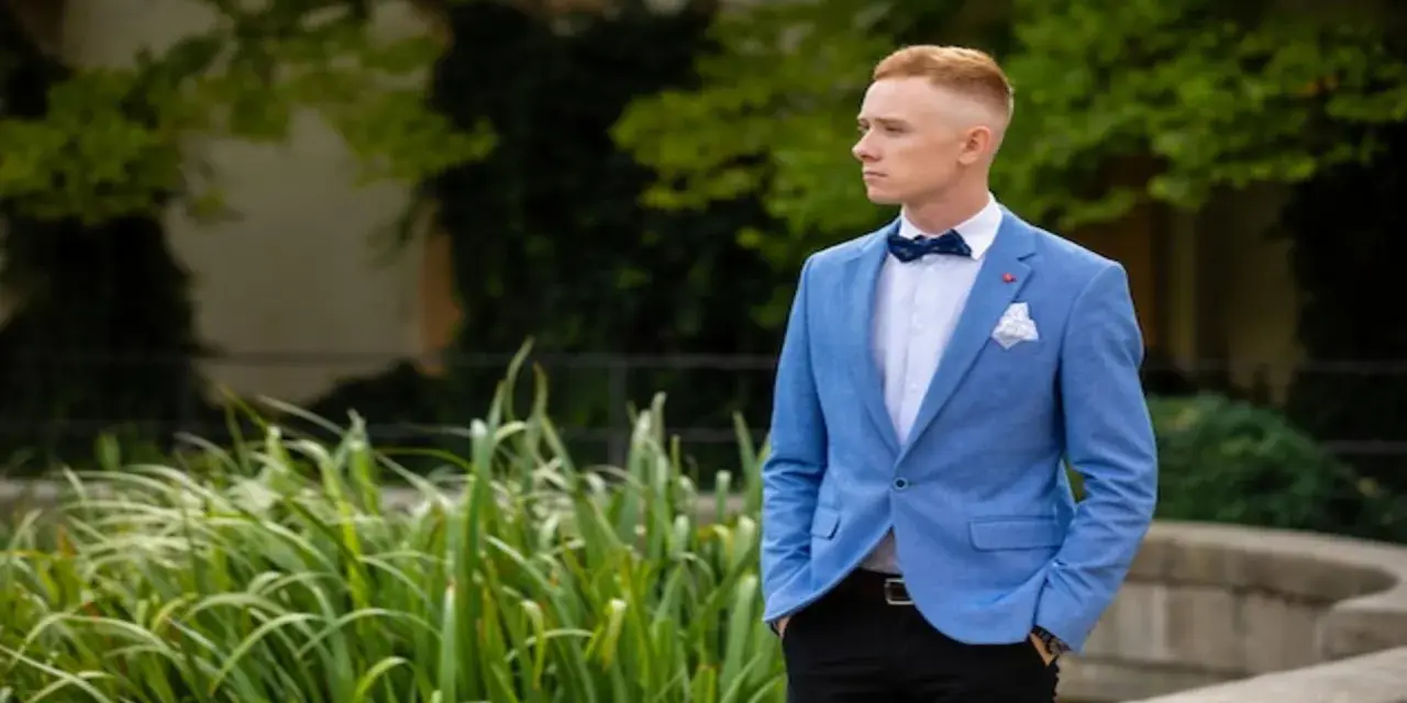 Elegancki mężczyzna w niebieskiej marynarce i czarnych spodniach, z muszką. Idealna stylizacja, jak ubrać faceta na wesele bez garnituru.