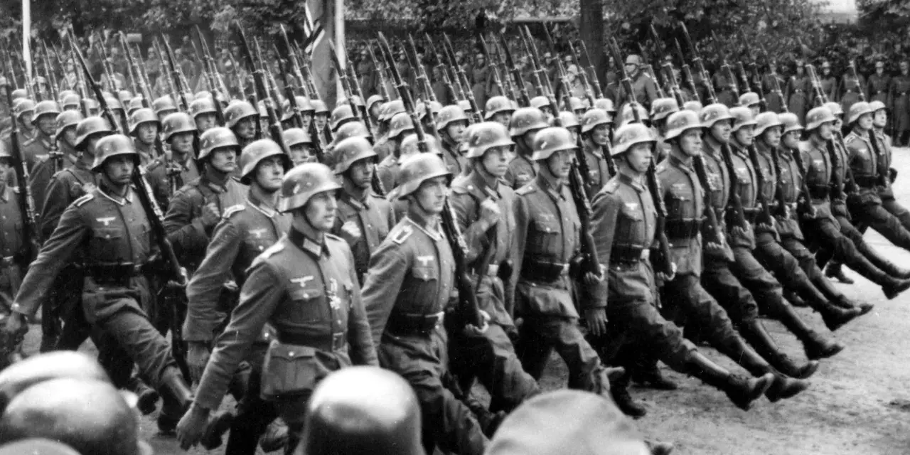 Żołnierze SS maszerują w zwartym szyku, niosąc karabiny. Ich charakterystyczne mundury, których projektant pozostaje nieznany, budzą grozę.