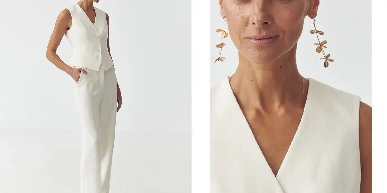 Elegancka kobieta w białej kamizelce bez marynarki i spodniach. Długie, złote kolczyki dodają stylizacji szyku.
