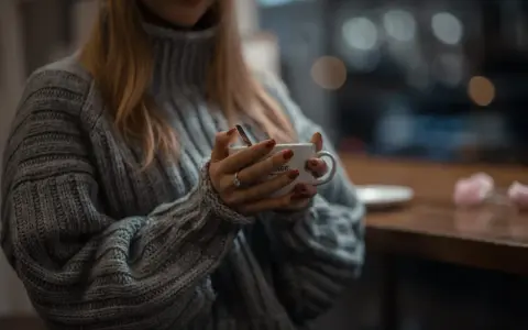 Mięciutki sweter z **lambswool** otula dłonie trzymające kubek. Czy taki materiał **gryzie**? Raczej nie, wygląda na bardzo komfortowy.