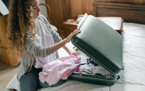 Kobieta pakuje różową koszulę do zielonej walizki, ucząc się, jak złożyć koszulę do walizki, by zaoszczędzić miejsce.
