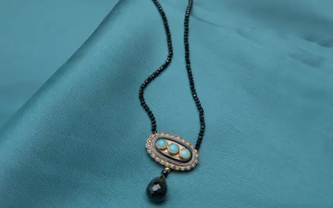 Elegancki naszyjnik z czarnego spinelu, ozdobiony owalnym medalionem z trzema niebieskimi kamieniami i wiszącą, czarną łezką.