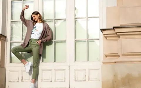 Elegancka kobieta w brązowym kardiganie i zielonych spodniach pokazuje, jak nosić kardigan na co dzień.