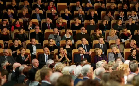 Elegancko ubrani ludzie siedzą w filharmonii, gotowi na koncert. Wskazówka, jak ubrać się do filharmonii: klasyka i szyk.