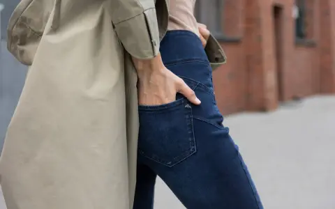 Kobieta w beżowym płaszczu i granatowych jeansach bootcut. Stylowe jeansy bootcut to podstawa wielu udanych stylizacji.