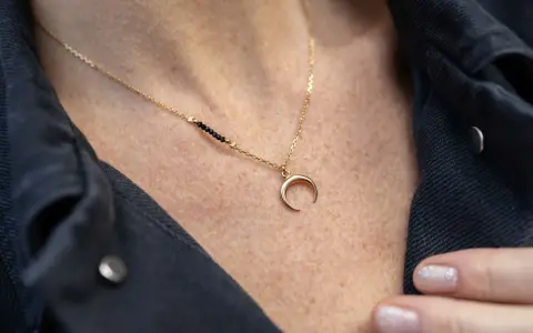 Złoty naszyjnik z zawieszką w kształcie rogalika księżyca i czarnymi koralikami. Co oznacza naszyjnik księżyc? Symbolizuje intuicję i kobiecą moc.