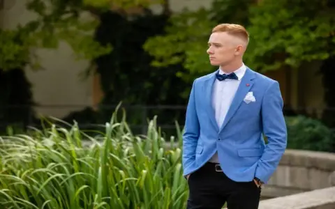 Elegancki mężczyzna w niebieskiej marynarce i czarnych spodniach, z muszką. Idealna stylizacja, jak ubrać faceta na wesele bez garnituru.