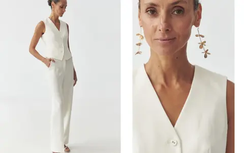 Elegancka kobieta w białej kamizelce bez marynarki i spodniach. Długie, złote kolczyki dodają stylizacji szyku.