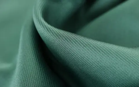 Gładka, zielona tkanina tencel, co to za materiał? Miękki, lejący się materiał z widocznym drobnym splotem.