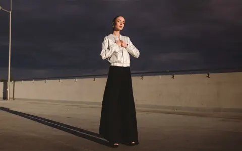 Elegancka bomberka stylizacje z długą czarną spódnicą. Kobieta pozuje na tle burzowego nieba.