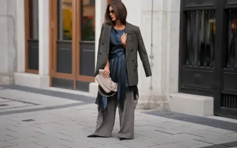 Elegancka stylizacja na kolację firmową: luźne spodnie, satynowa sukienka z koronką, marynarka i torebka.
