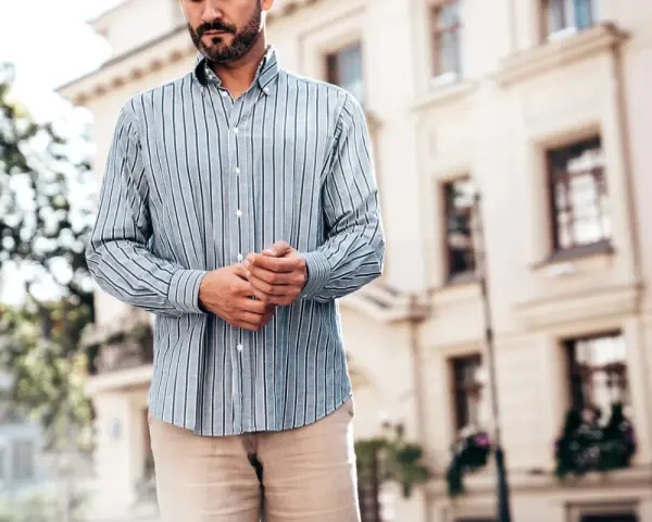 Mężczyzna w pasiowanej koszuli i beżowych spodniach. Stylizacja: koszula w spodnie czy nie? Elegancko i swobodnie.