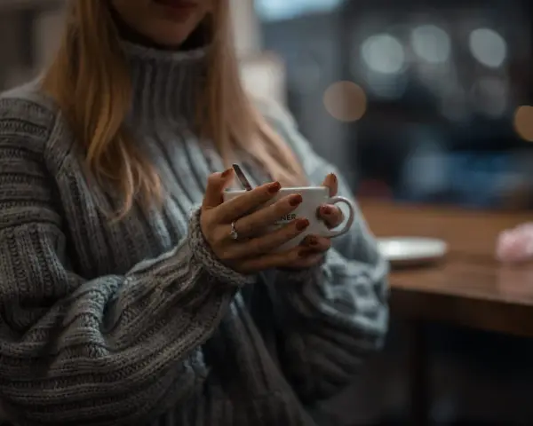 Mięciutki sweter z **lambswool** otula dłonie trzymające kubek. Czy taki materiał **gryzie**? Raczej nie, wygląda na bardzo komfortowy.