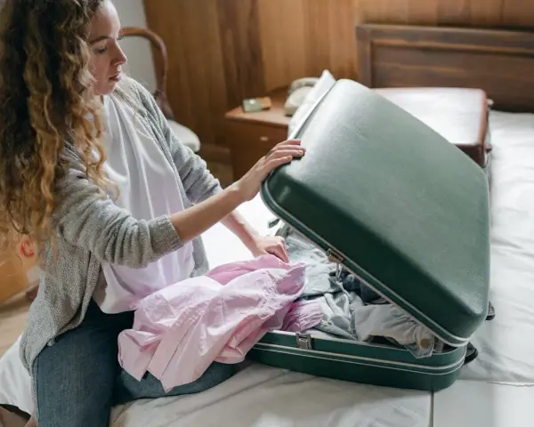 Kobieta pakuje różową koszulę do zielonej walizki, ucząc się, jak złożyć koszulę do walizki, by zaoszczędzić miejsce.