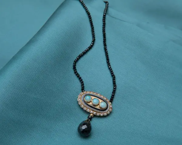 Elegancki naszyjnik z czarnego spinelu, ozdobiony owalnym medalionem z trzema niebieskimi kamieniami i wiszącą, czarną łezką.