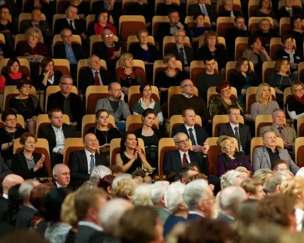 Elegancko ubrani ludzie siedzą w filharmonii, gotowi na koncert. Wskazówka, jak ubrać się do filharmonii: klasyka i szyk.