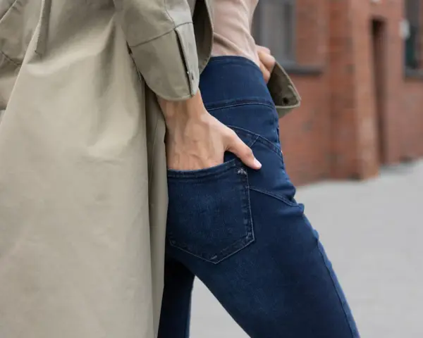 Kobieta w beżowym płaszczu i granatowych jeansach bootcut. Stylowe jeansy bootcut to podstawa wielu udanych stylizacji.