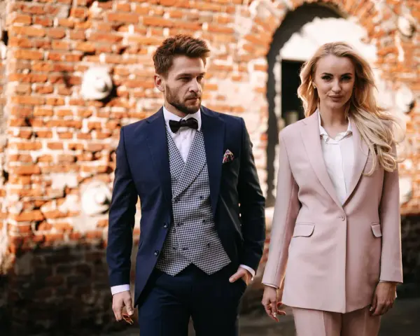Elegancka para w strojach na komunię dziecka. On w granatowym garniturze, ona w pudrowym.