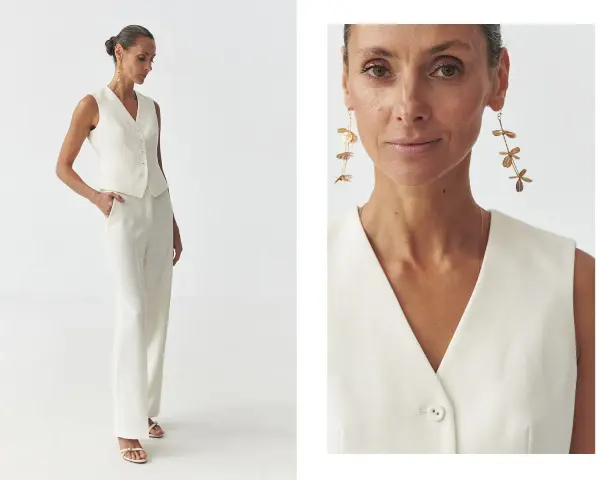 Elegancka kobieta w białej kamizelce bez marynarki i spodniach. Długie, złote kolczyki dodają stylizacji szyku.