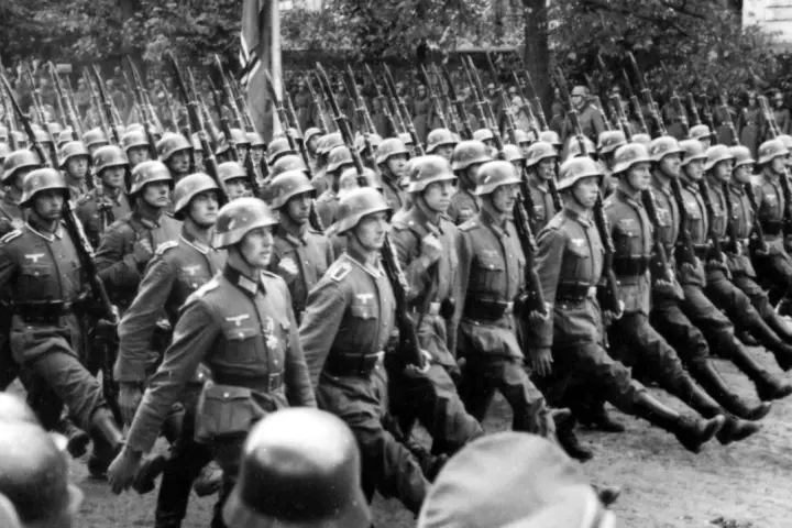 Żołnierze SS maszerują w zwartym szyku, niosąc karabiny. Ich charakterystyczne mundury, których projektant pozostaje nieznany, budzą grozę.