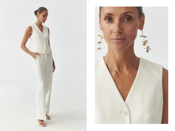Elegancka kobieta w białej kamizelce bez marynarki i spodniach. Długie, złote kolczyki dodają stylizacji szyku.
