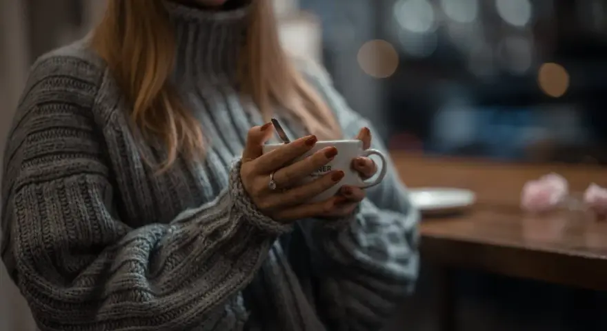 Mięciutki sweter z **lambswool** otula dłonie trzymające kubek. Czy taki materiał **gryzie**? Raczej nie, wygląda na bardzo komfortowy.