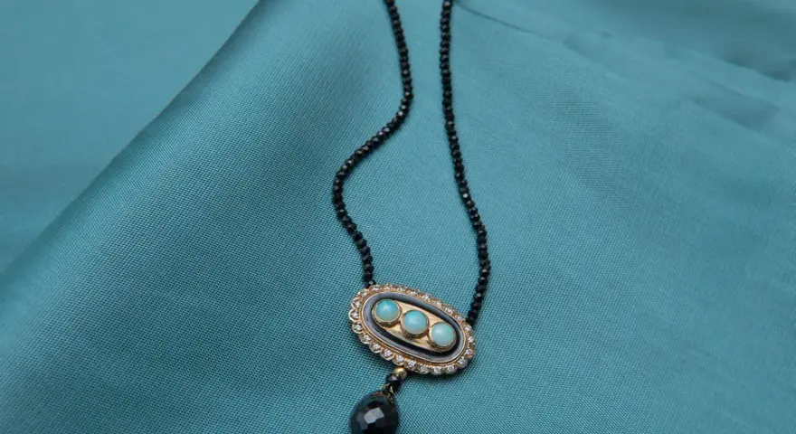 Elegancki naszyjnik z czarnego spinelu, ozdobiony owalnym medalionem z trzema niebieskimi kamieniami i wiszącą, czarną łezką.