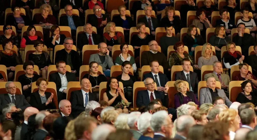 Elegancko ubrani ludzie siedzą w filharmonii, gotowi na koncert. Wskazówka, jak ubrać się do filharmonii: klasyka i szyk.