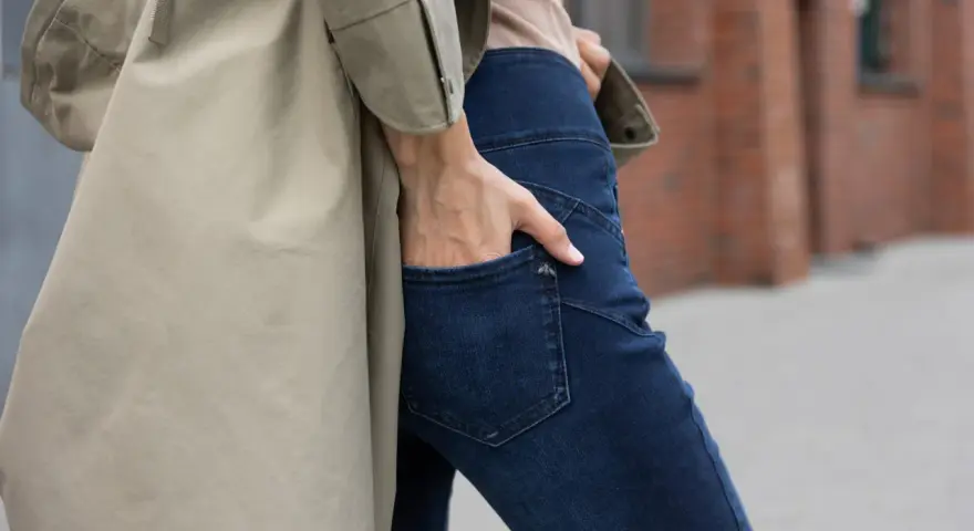 Kobieta w beżowym płaszczu i granatowych jeansach bootcut. Stylowe jeansy bootcut to podstawa wielu udanych stylizacji.