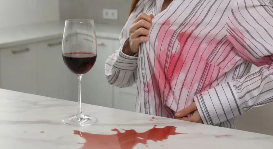 Kobieta pokazuje dużą plamę z czerwonego wina na swojej białej koszuli. Dowiedz się, jak usunąć plamę z wina.