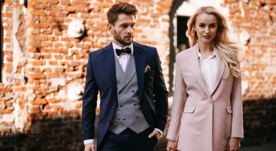 Elegancka para w strojach na komunię dziecka. On w granatowym garniturze, ona w pudrowym.